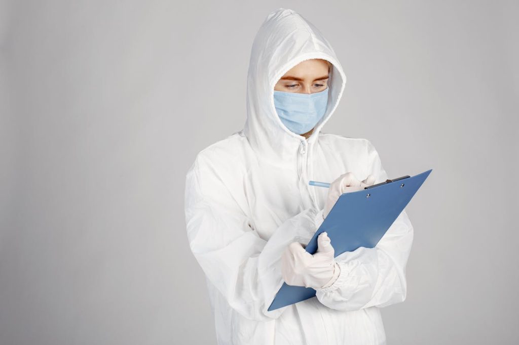 portrait-of-a-doctor-in-a-protective-clothing-5934368 Healthcare professional in PPE suit writing on clipboard in a clinical setting.
