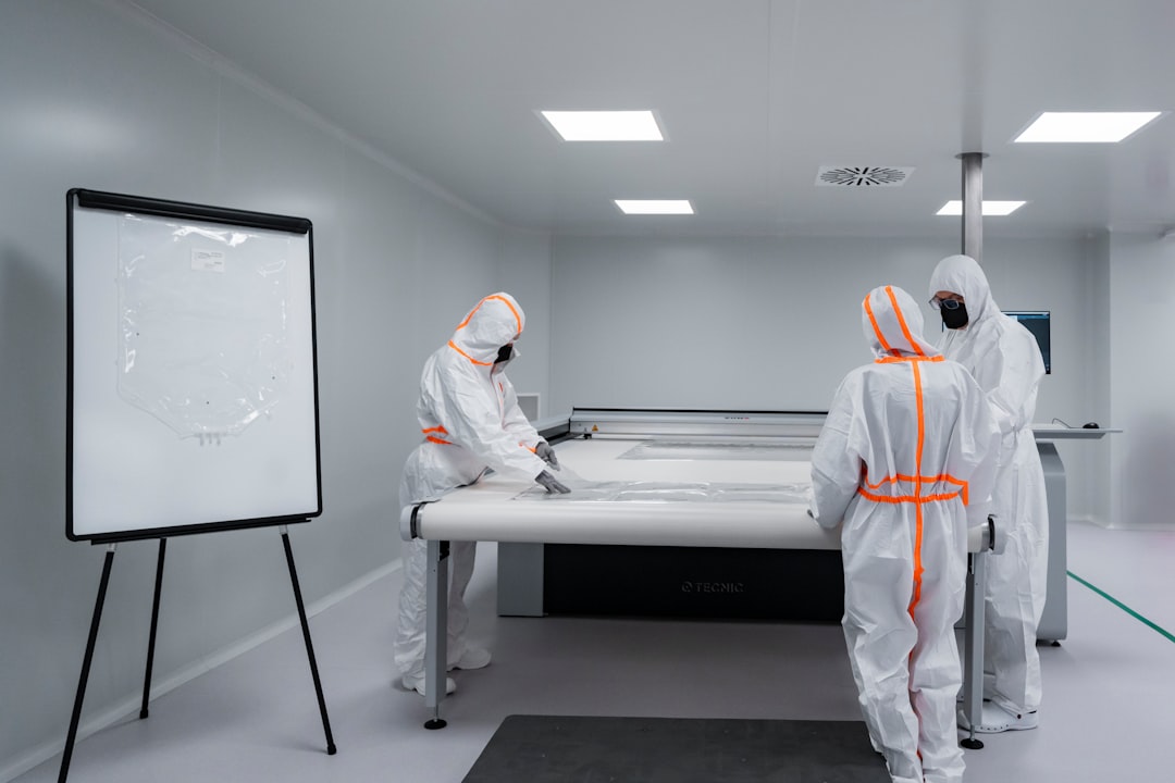 Three operators in cleanroom suits preparing and inspecting single-use bag materials on a flat surface inside a sterile cleanroom.